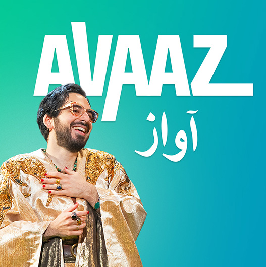The image features writer and performer Michael Shayan, a man with a beard and glasses, depicted from the waist up, against a gradient background that transitions from green on the left to teal on the right. The person is wearing a luxurious, gold robe garment with wide sleeves and gold, glittering embroidery on the shoulders. They are standing with their left hand rested on their chest while their right hand is folded below, giving a gesture that suggests they might be laughing or smiling. Large white text depicting the name of the production is displayed prominently on the right side of the image, with a smaller text in Arabic script beneath it.