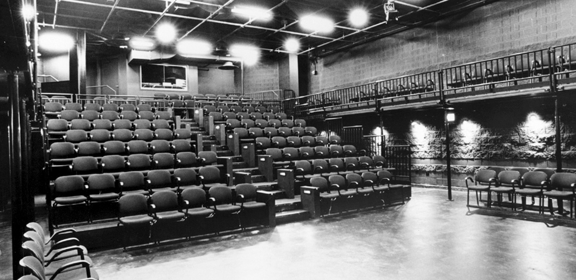 Black and white photo of a modern theater with tiered seating, balcony seating, and industrial-style design.