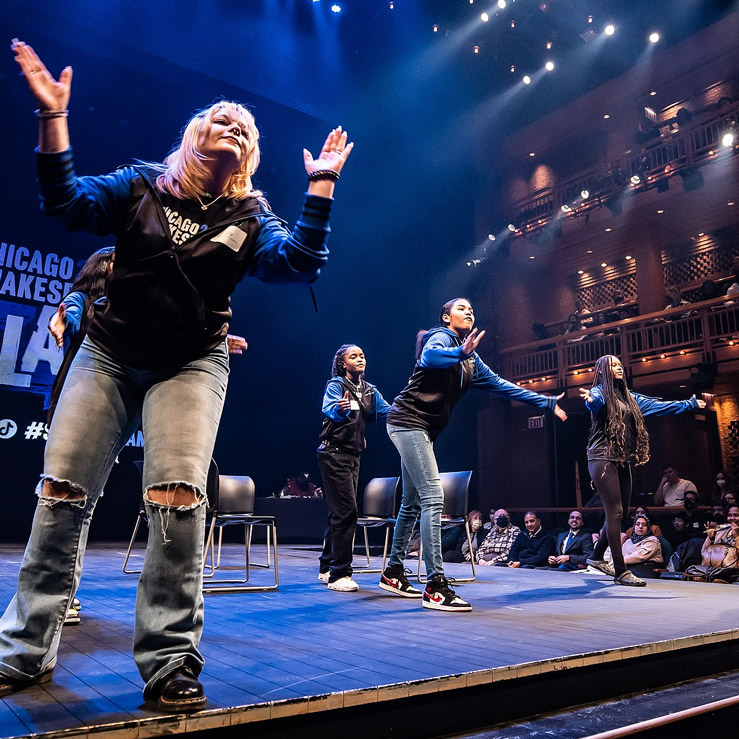 Group of five performers on stage gesturing for audience members to clap along during the Chicago Shakespeare SLAM in the Courtyard Theater.