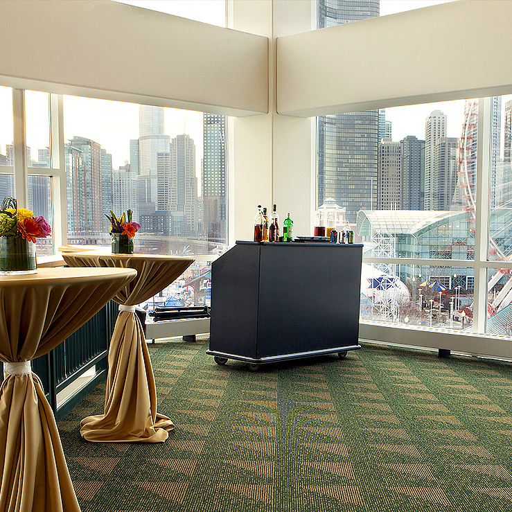 Top floor indoor event space at Chicago Shakespeare with high-top tables and a portable bar with the Chicago skyline visible through large windows.