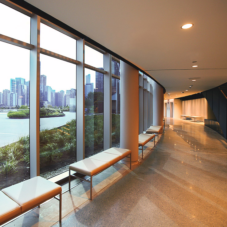 Interior hallway of The Yard with floor-to-ceiling windows, cushioned benches, polished floors, and a city skyline view of Chicago.