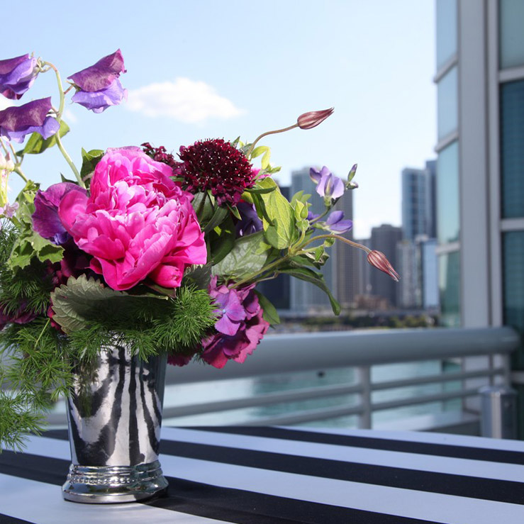 Bouquet of colorful flowers in a silver vase on a table with a black and white striped tablecloth, with the Chicago skyline in the background.