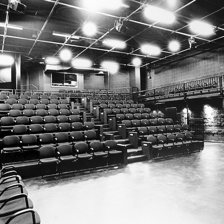 Black and white photo of a modern theater with tiered seating, balcony seating, and industrial-style design.