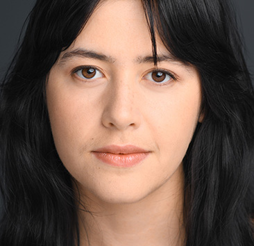 Headshot of a person with long, straight, dark hair and brown eyes against a dark gray background.