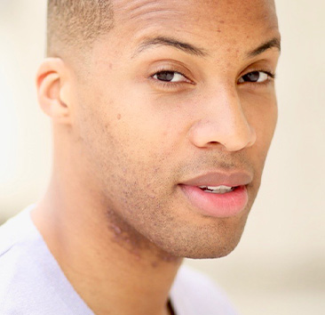 Close-up portrait of a young person with short hair, a slight smile, and brown eyes.