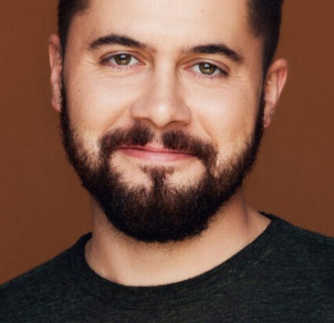 Close-up portrait of a person with a beard smiling against a brown background