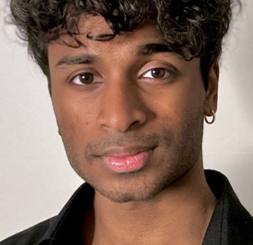 Headshot of a young person with curly black hair, wearing a black shirt and a small hoop earring