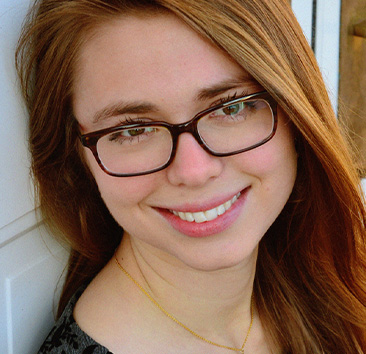 Close-up portrait of a person with light, reddish-brown hair, wearing glasses, and smiling.