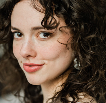 Close-up of a person with dark curly hair, and dark eyes, slightly smiling.