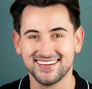 Close-up portrait of a smiling person with short, dark hair and a teal background