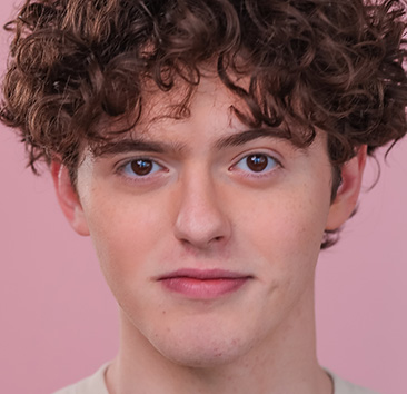 Close-up portrait of a person with short, curly hair against a solid light pink background