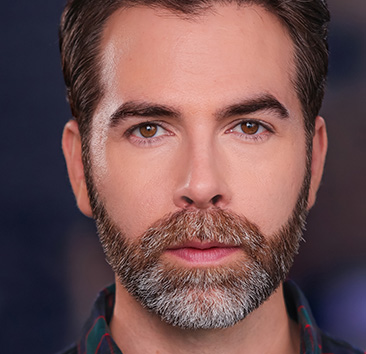 Close-up portrait of a person with a beard and brown eyes against a blurred dark background