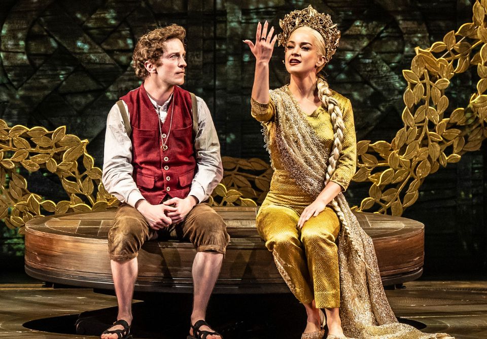 Frodo in a red vest and brown pants on left and Galadrial in a gold outfit sit on raised platform, with Galadrial's right hand outstretched looking at a ring on her finger